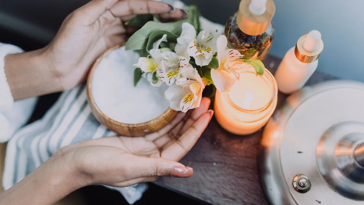 Hands holding a skincare jar among candles and fresh flowers